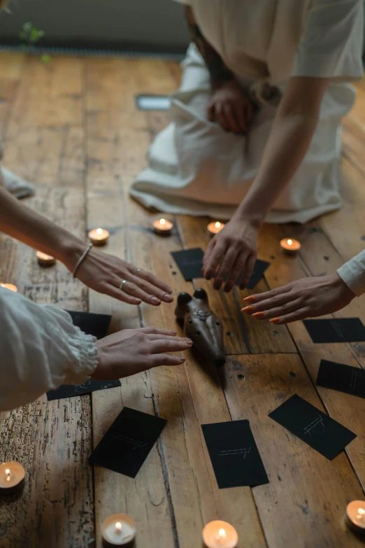 a group of people sitting on top of a wooden floor, a seance, four hands, chalk, white candles