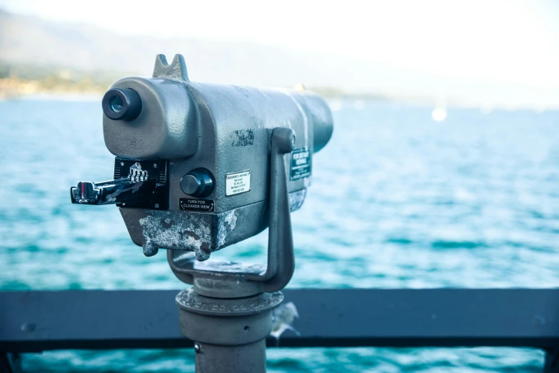 a close up of a telescope near a body of water, by Niko Henrichon, unsplash, visual art, near a jetty, looking at camera, seaview, with laser-like focus