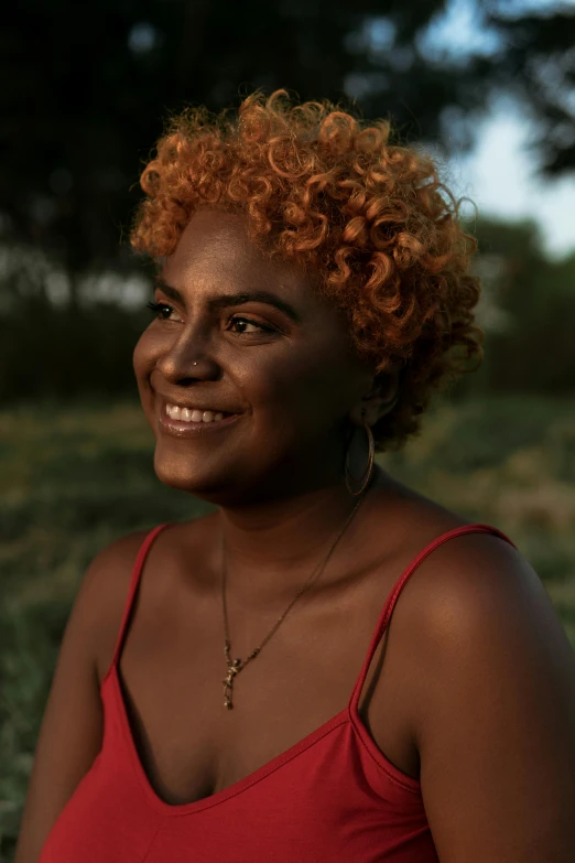 a woman in a red tank top standing in a field, by Lily Delissa Joseph, orange glowing hair, 30-year-old woman from cuba, profile image, dark short curly hair smiling