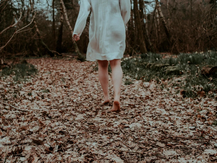 a woman in a white dress walking in the woods, an album cover, pexels contest winner, bare legs, brown clothes, background image, creepy aesthetic