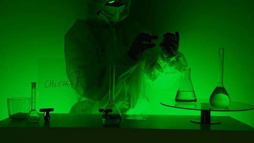 a person wearing a mask standing in front of a green light, pexels, holography, scientific glassware, reagents, back lighting, chemisty