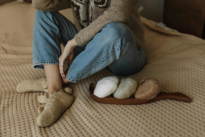 a woman sitting on top of a bed next to a pair of slippers, inspired by Sarah Lucas, trending on pexels, fibres trial on the floor, brown and cream color scheme, wearing jeans, cottagecore