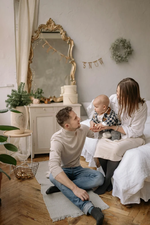 a man and woman sitting on a bed with a baby, by Adam Marczyński, pexels contest winner, renaissance, cozy home background, on a white table, decorations, happy kid