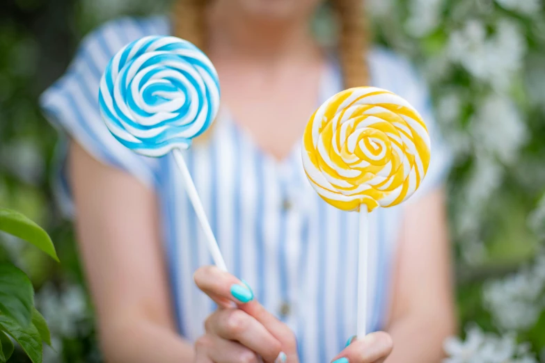 a woman holding two lollipops in her hands, inspired by Dod Procter, pexels contest winner, yellow and blue and cyan, spiral, avatar image, outdoor photo