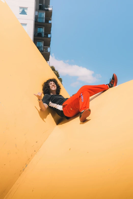 a man riding a skateboard down the side of a yellow ramp, an album cover, by Nathalie Rattner, trending on pexels, wearing red and yellow clothes, laying on her back, zack de la rocha, high in the sky