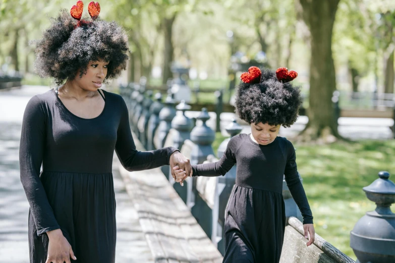 a woman and a child walking in a park, an album cover, pexels contest winner, black arts movement, giant red carnation afro head, humans of new york style, she is wearing a black dress, beautiful gemini twins