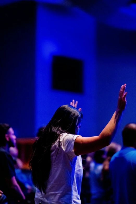 a woman standing in front of a crowd of people, pray, dramatic blue lighting, raised hand, college