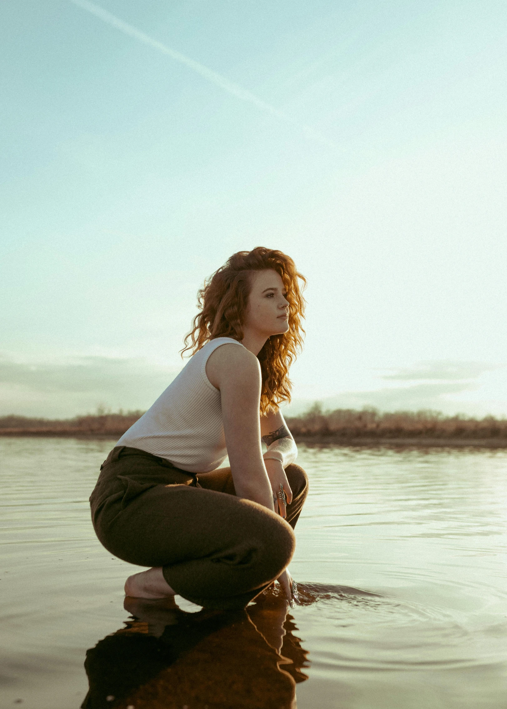 a woman kneeling on top of a body of water, an album cover, trending on pexels, a redheaded young woman, looking to the side off camera, spring season, curly haired