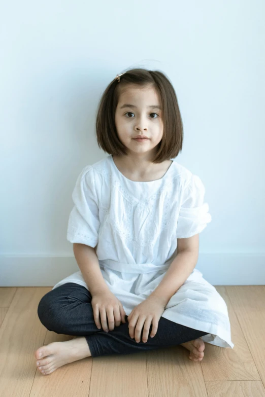 a little girl sitting on the floor with her legs crossed, wearing a white shirt, medium portrait top light, lulu chen, full product shot