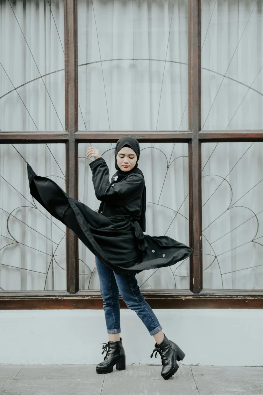 a woman standing in front of a window holding an umbrella, inspired by Bernardino Mei, pexels contest winner, arabesque, wearing jeans and a black hoodie, hero action pose, islamic, long shirt