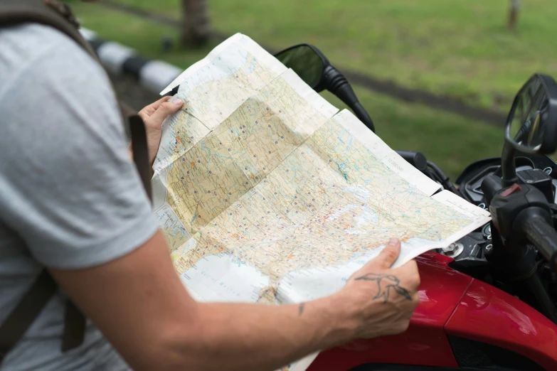 a man sitting on a motorcycle holding a map, unsplash, rectangle, tourist map, close - up photograph, colour photograph