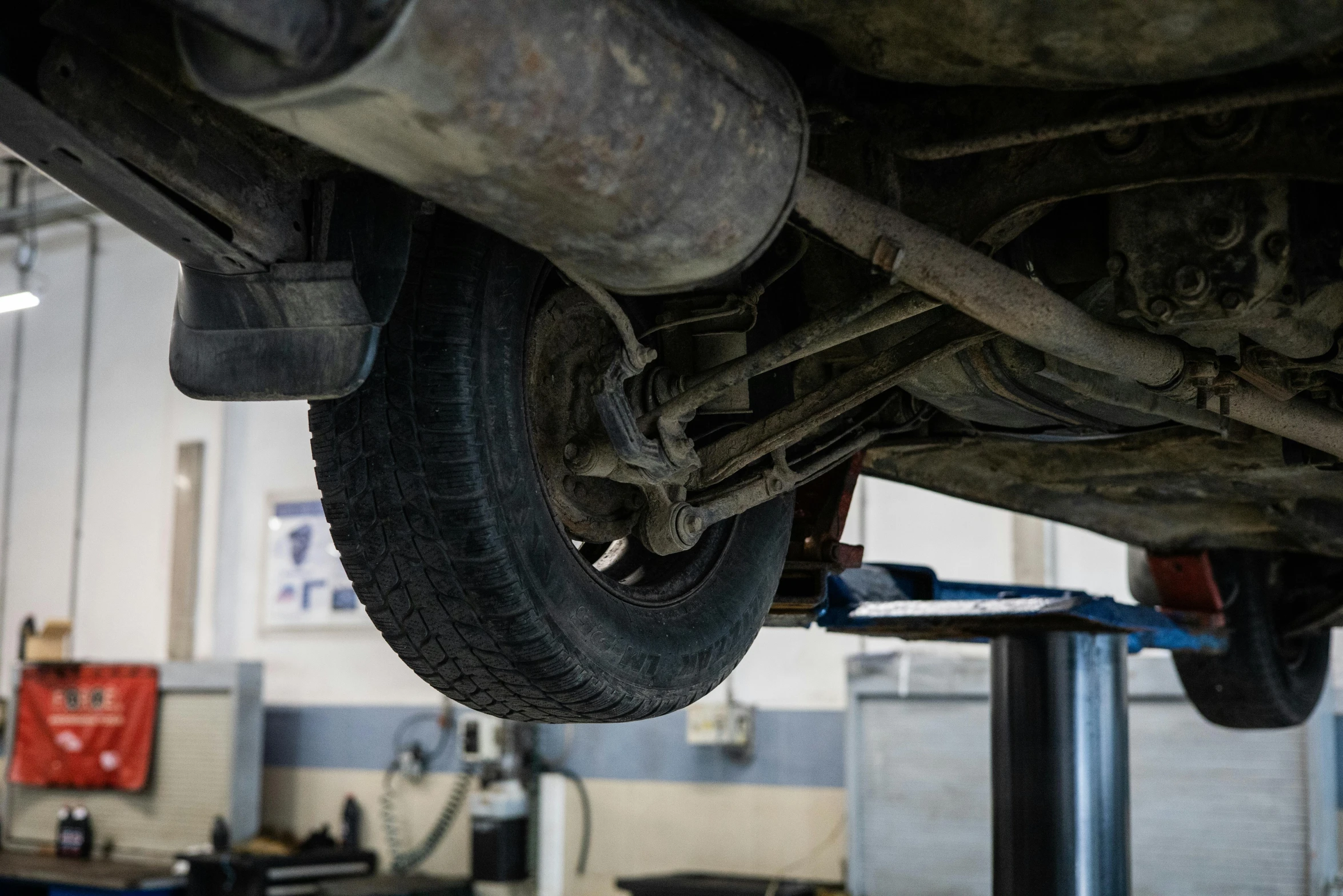 a close up of a car in a garage, underbody, knees upturned, metal works, half turned around