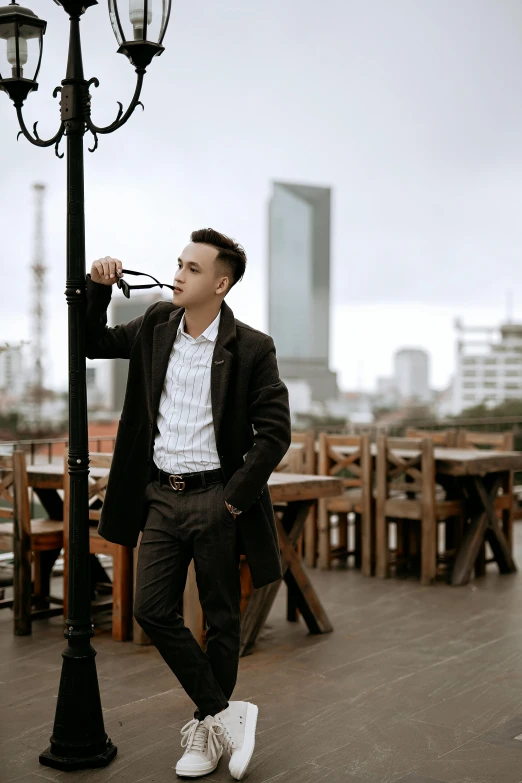 a man standing on top of a wooden floor next to a lamp post, by Robbie Trevino, pexels contest winner, in style of lam manh, wearing a fancy jacket, at the terrace, wearing business casual dress