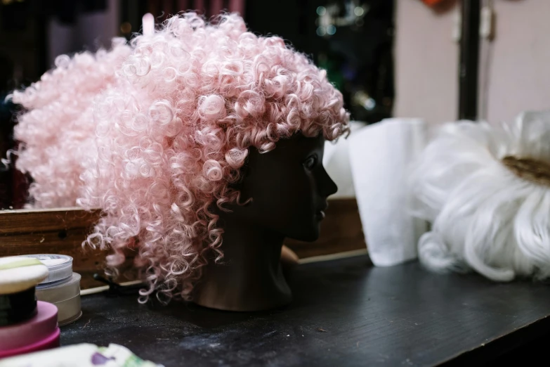 a pink wig sitting on top of a table, trending on pexels, plasticien, curly haired, in a workshop, headpiecehigh quality, great likeness
