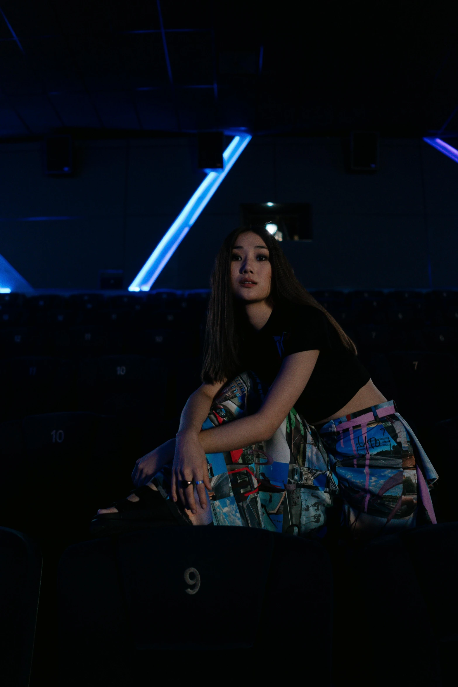 a woman sitting on top of a suitcase in a dark room, inspired by Feng Zhu, holography, sitting in a movie theater, she is wearing streetwear, slide show, hollywood promotional image