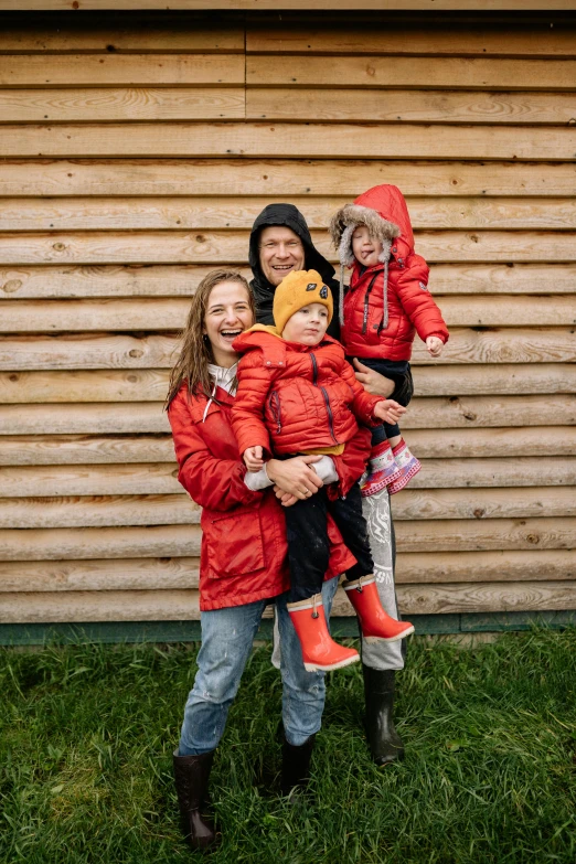 a family poses for a picture in front of a barn, inspired by The Family Circus, pexels contest winner, incoherents, girl in raincoat, red sport clothing, model wears a puffer jacket, twins