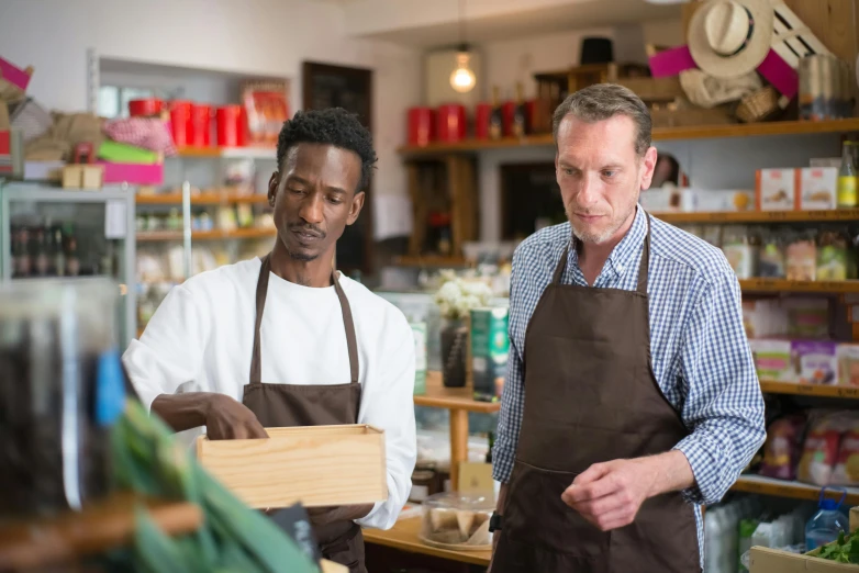 a couple of men standing next to each other in a store, by Julian Hatton, pexels, renaissance, on a wooden tray, people at work, brown, facebook post