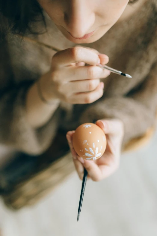 a close up of a person holding an egg, an airbrush painting, pexels contest winner, arts and crafts movement, decorative ornaments, holding brush, jovana rikalo, creating a soft