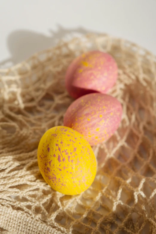three yellow and pink easter eggs in a net bag, inspired by Peter Alexander Hay, trending on pexels, gold speckles, smooth matte, chalk, mango