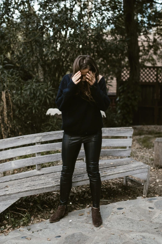 a woman standing on top of a wooden bench, by Lucia Peka, trending on unsplash, happening, black sweater, facepalm, black leather shiny jeans, distraught