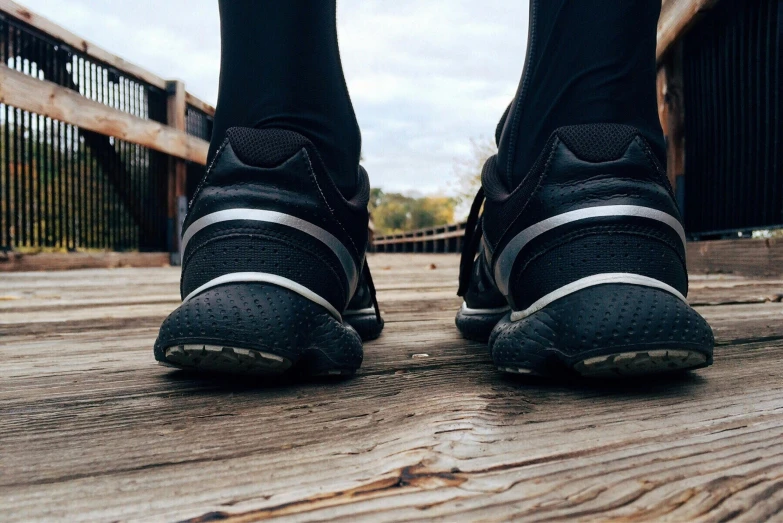 a close up of a person's shoes on a wooden bridge, wearing fitness gear, from the back, profile image, thumbnail