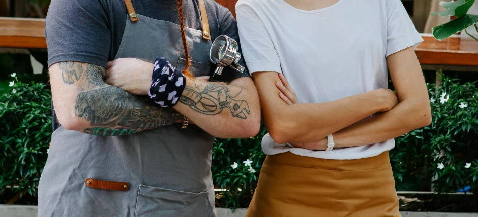 a man and a woman standing next to each other, a tattoo, by Tom Bonson, pexels contest winner, aussie baristas, plated arm, exterior shot, angie glocka