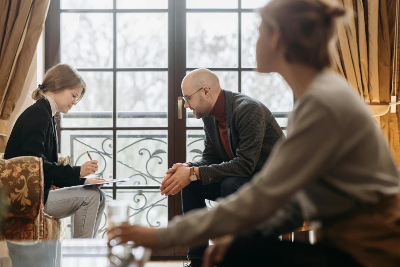 a man and a woman sitting in front of a window, unsplash, group sit at table, realistic »