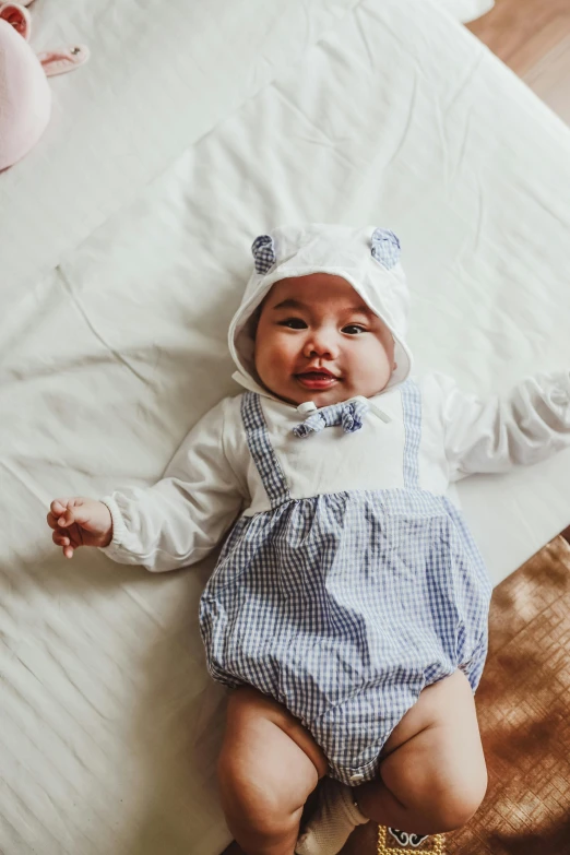 a baby laying on top of a bed next to a teddy bear, by Julia Pishtar, sailor clothing, costume with blue accents, lifestyle, overalls