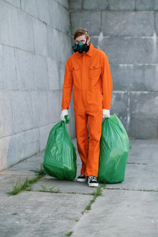 a man in an orange coverall holding two green bags, by Andries Stock, pexels contest winner, arte povera, sweeping, prison jumpsuit, disposal mummy, 🦑 design