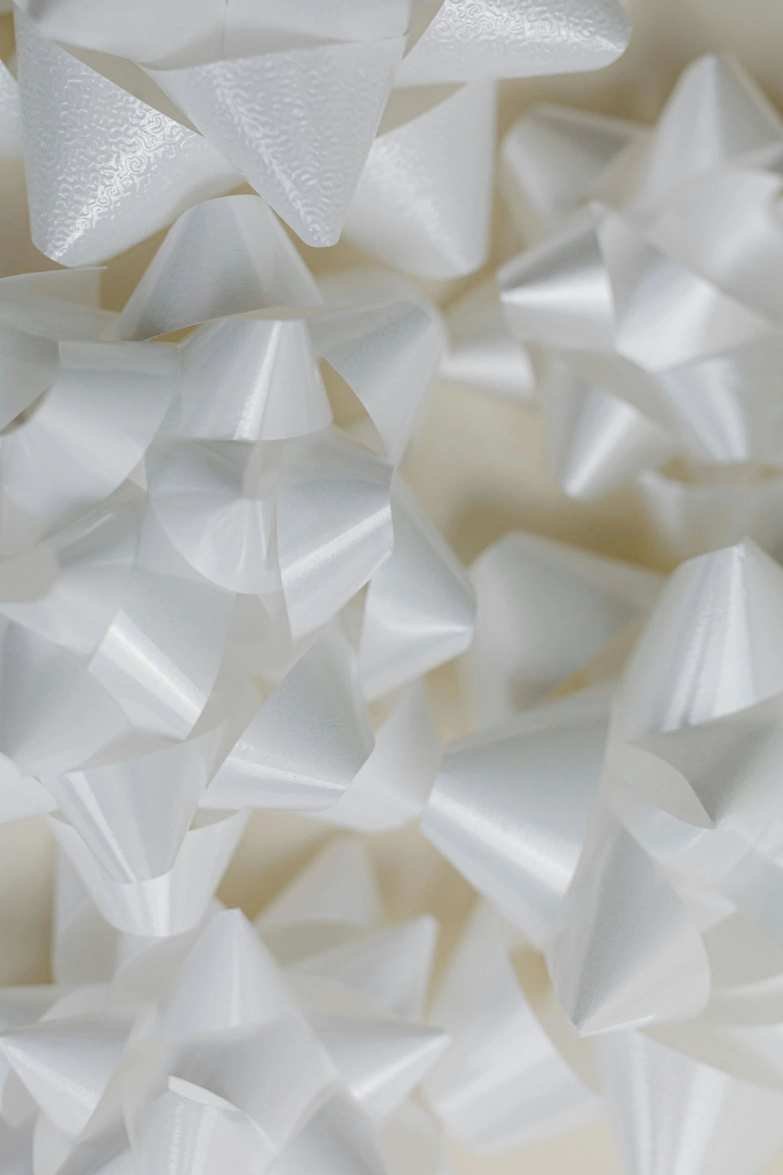 a pile of white ribbons sitting on top of a table, inspired by Cornelia Parker, reddit, plasticien, fractal detail, resin coated, peaks, bowknot