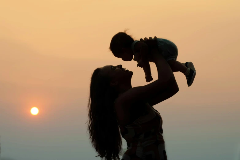 a woman holding a baby up in the air, pexels contest winner, symbolism, in a sunset haze, profile image, tourist photo, profile pic
