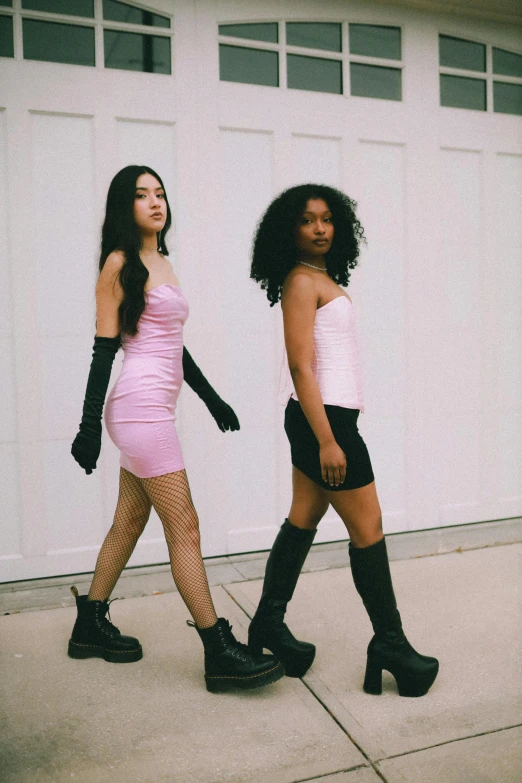 two women walking in front of a garage door, an album cover, inspired by Wang Duo, trending on pexels, renaissance, pink body harness, high boots, mixed race, black and pink dress