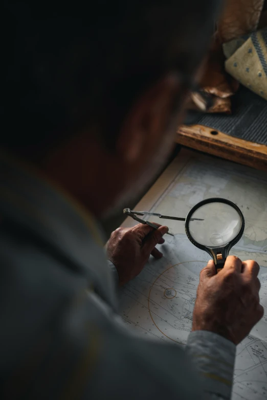 a man is looking through a magnifying glass, an etching, pexels contest winner, shipibo patterns, in a workshop, birdseye view, charts