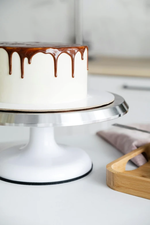 a cake sitting on top of a white cake plate, by Julia Pishtar, unsplash, stainless steal, brown and white color scheme, drip, product introduction photo