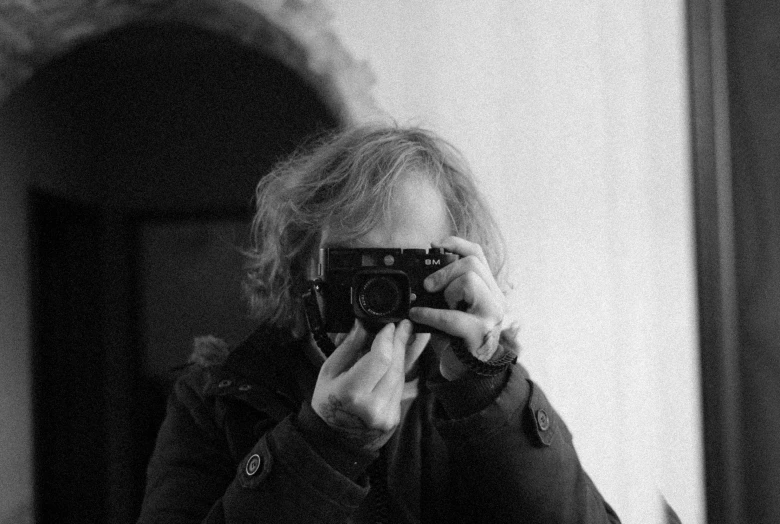 a woman taking a picture of herself in a mirror, a black and white photo, inspired by Henri Cartier-Bresson, unsplash, visual art, vito acconci, holding a camera, is looking at the camera, mana shooting from his hands