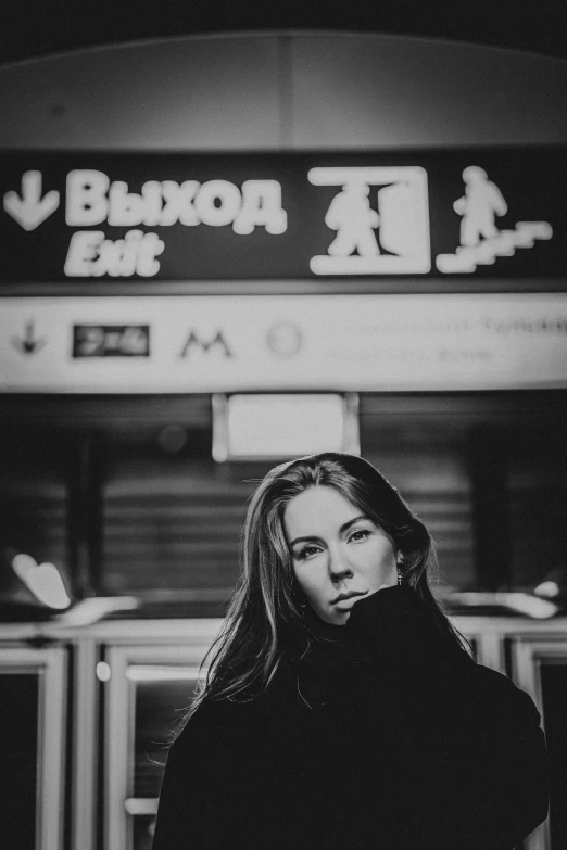 a woman standing in front of a train station, a black and white photo, by Alexey Venetsianov, pexels contest winner, with neon signs, ((portrait)), beautiful lonely girl, bus stop