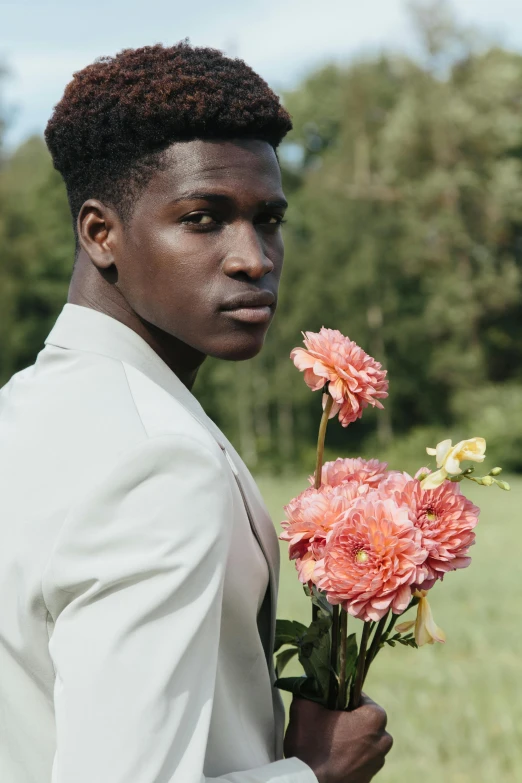 a man standing in a field holding a bunch of flowers, by Carey Morris, trending on unsplash, romanticism, black teenage boy, groom, off - white collection, made of flowers