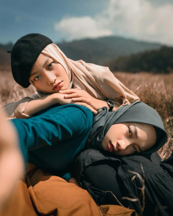 a man and a woman laying in a field, a picture, by Basuki Abdullah, trending on unsplash, sumatraism, non binary model, hijab, woman holding another woman, staring at the viewer