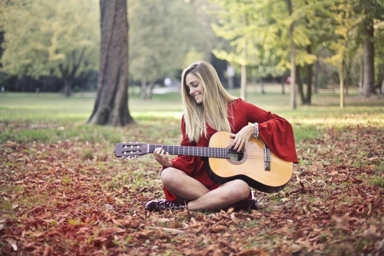 a woman sitting on the ground playing a guitar, pexels, avatar image, fall season, girl wears a red dress, a blond