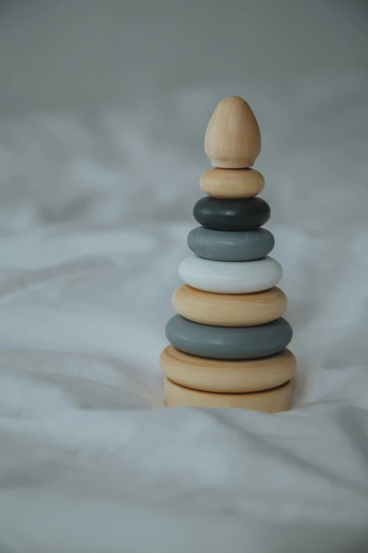 a stack of rocks sitting on top of a bed, by Eleanor Best, childrens toy, rings, grey colours, spire