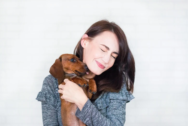 a woman holding a dog in her arms, inspired by Elke Vogelsang, pexels contest winner, portrait of a dachshund, white background and fill, brunette, youtube thumbnail