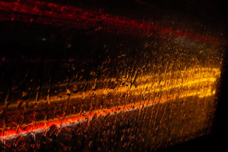 a close up of a window with rain on it, an album cover, by Thomas Häfner, pexels contest winner, lyrical abstraction, orange and red lighting, traffic with light trails, shining gold and black and red, small streaks of light through