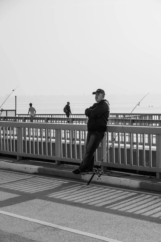 a man riding a skateboard across a bridge, a black and white photo, happening, fishing pole, at the seaside, sittin, looking content