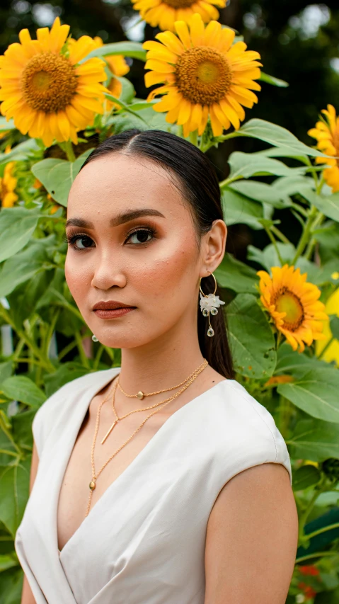 a woman standing in front of a field of sunflowers, inspired by Ruth Jên, pexels contest winner, sumatraism, earrings, pearls and gold chains, fashion model features, wearing several pendants