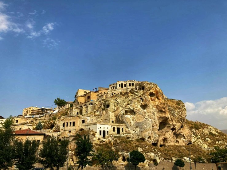 a group of buildings sitting on top of a mountain, by Muggur, ancient caves, blue sky, instagram photo, front view