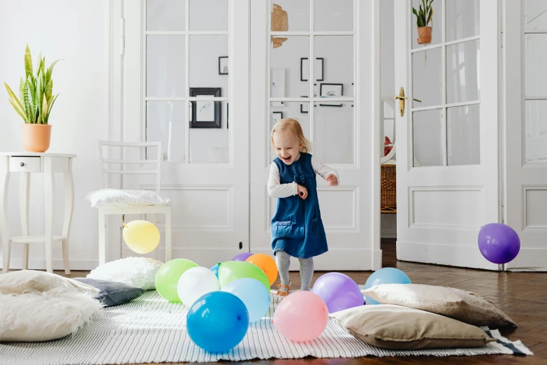 a little girl standing in front of a bunch of balloons, an album cover, by The Family Circus, pexels contest winner, in a living room, activity play centre, location in a apartment, hygge