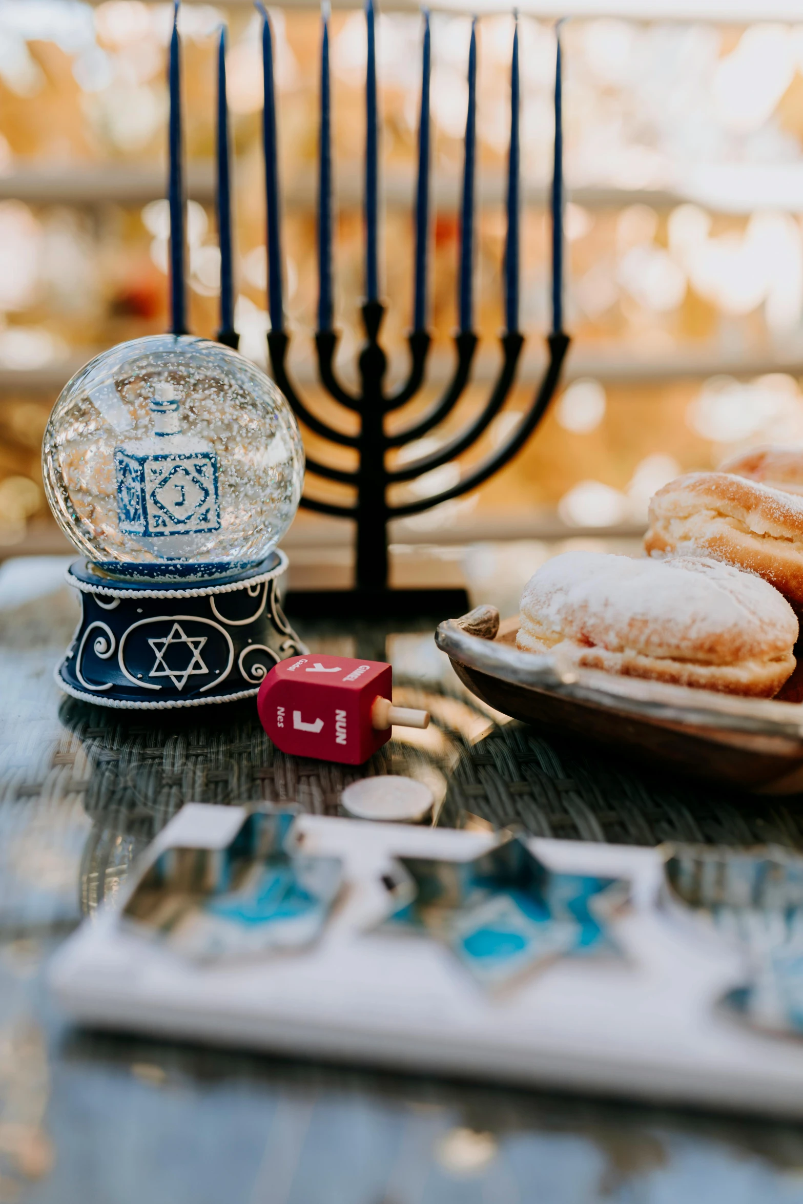 a table topped with a plate of doughnuts next to a menorah, snow globe, a close up shot, symbols, square