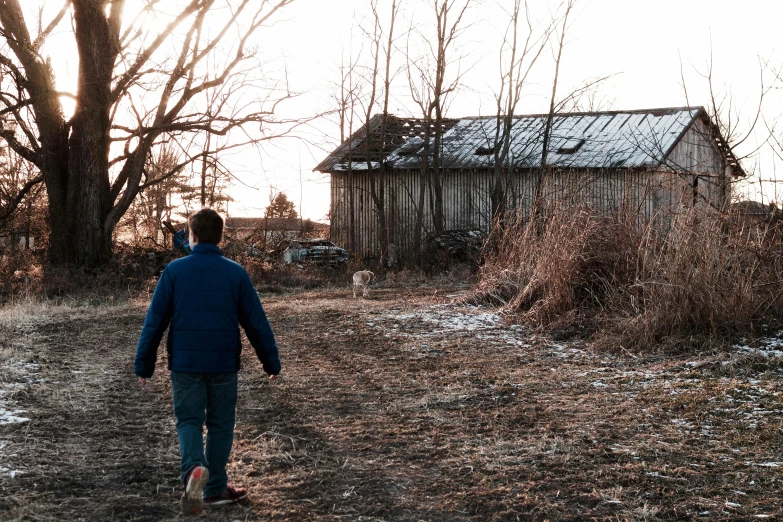 a man walking down a dirt road towards a barn, an album cover, by Adam Marczyński, pexels contest winner, photo of poor condition, late afternoon, in front of the house, promo image