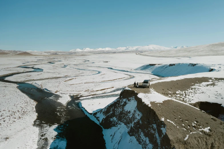 a group of people standing on top of a snow covered mountain, by Muggur, with a river running through it, vehicle, 4k image”