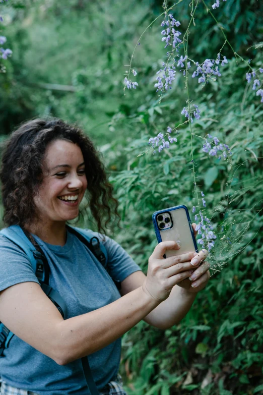 a woman taking a picture of a purple flower, happening, wearing adventuring gear, vines and blue foliage, she is smiling and excited, profile image